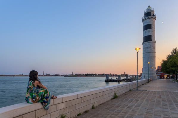A woman admires the lighthouse of Murano (the only one in Venice Lagoon), Murano Island, Venice, Veneto, Italy.