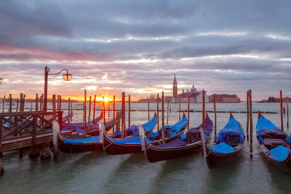 Some traditional venetian gondolas moored at Riva degli Schiavoni at dawn with St. george Island on the backgrund, Venice, Veneto, Italy.