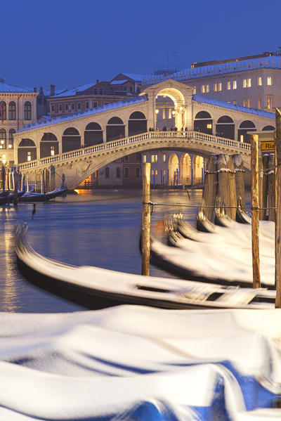 Rialto Bridge with snow-covered gondolas at dusk after a snowfall, Grand Canal, Venice, Veneto, Italy