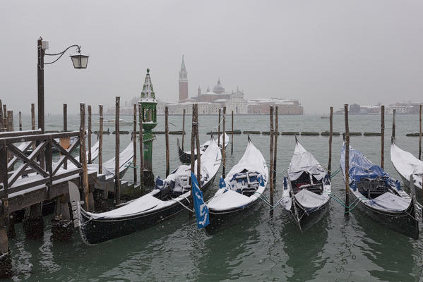 Some traditional venetian gondolas moored at Riva degli Schiavoni during a snowfall, Venice, Veneto, Italy