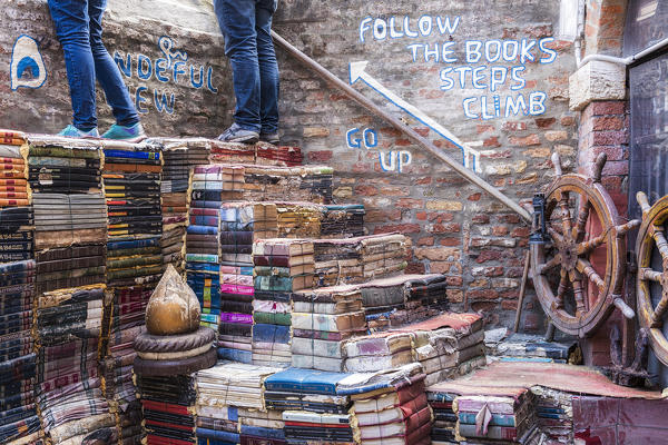 Tourists observe the canal from the steps created with books in the Acqua Alta bookshop, Venice, Veneto, Italy