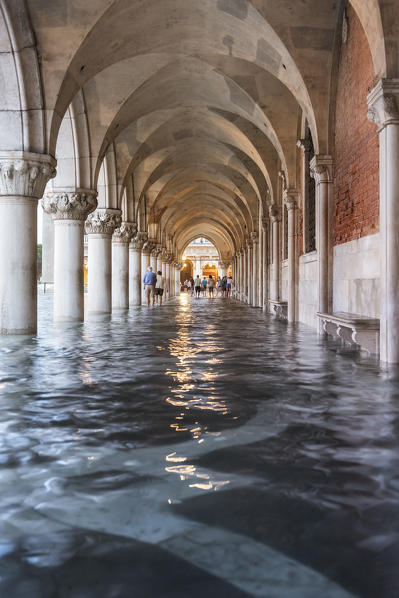 People walking in the high tide under the arches of the Doge's Palace, Venice, Veneto, Italy
