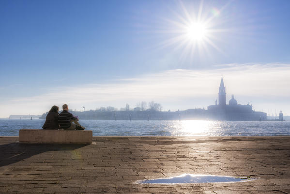 Couple of tourists observe the St. George's island from Riva degli Schiavoni, Venice, Veneto, Italy