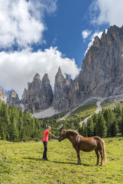 Tiers / Tires, Tires Valley, province of Bolzano, Dolomites, South Tyrol, Italy. A girl strokes a horse in front of the Vaiolet Towers