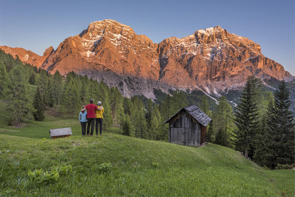 La Valle / Wengen, Alta Badia, Bolzano province, South Tyrol, Italy. Hikers admire the Enrosadira in the rocks of the mountains Cima Nove / Neunerspitze and Cima Dieci / Zehnerspitze