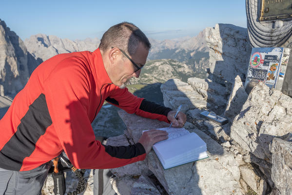 Sesto / Sexten, province of Bolzano, Dolomites, South Tyrol, Italy. Mountaineer sign the summitbook of Mount Paterno