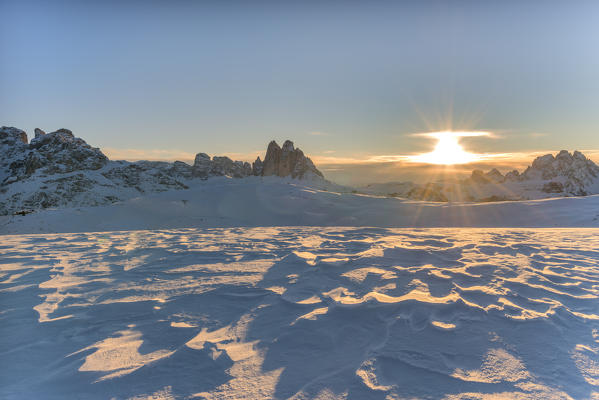 Prato Piazza/Plätzwiese, Dolomites, province of Bolzano, South Tyrol, Italy. Patterns in wind-eroded snow. In the background the rising sun and the famous peaks of Tre Cime di Lavaredo