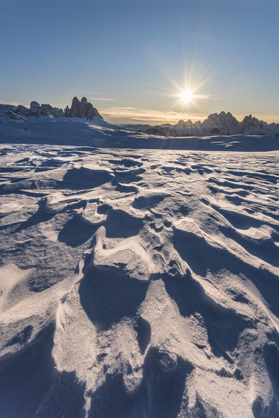 Prato Piazza/Plätzwiese, Dolomites, province of Bolzano, South Tyrol, Italy. Patterns in wind-eroded snow. In the background the rising sun and the famous peaks of Tre Cime di Lavaredo