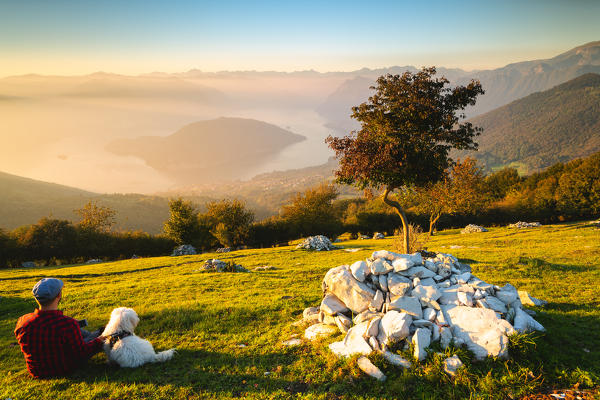 A person with his dog admire the sunset over Lake Iseo, Brescia province, Lombardy district, Italy.