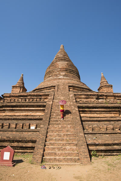 Bagan, Mandalay region, Myanmar (Burma). Woman walking on the steps of a stupa. MR.