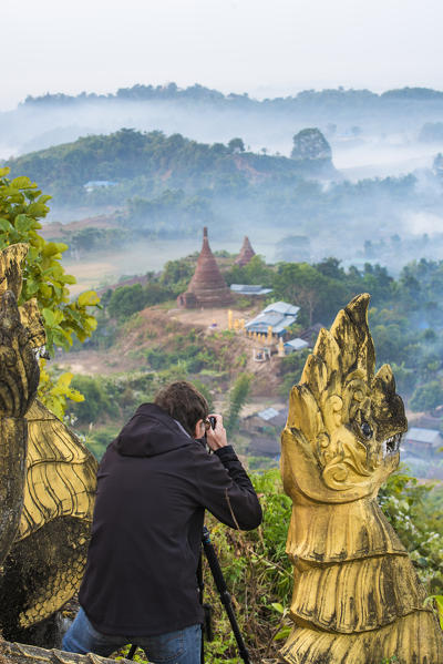 Mrauk-U, Rakhine state, Myanmar. Man taking pictures of Mrauk-U in a foggy sunrise from the Shwetaung pagoda.