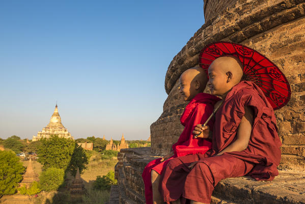 Bagan, Mandalay region, Myanmar (Burma). Two young monks sitting on top of a stupa with the Shwesandaw pagoda in the background.