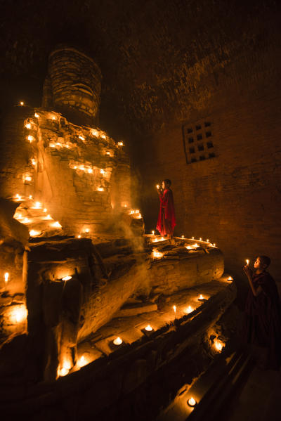 Bagan, Mandalay region, Myanmar (Burma). Young monks praying at a giant brick-make statue of the Buddha inside a small temple.