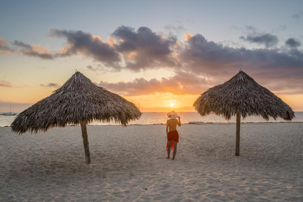 Bavaro Beach, Bavaro, Higuey, Punta Cana, Dominican Republic. Woman by thatch umbrellas on the beach at sunrise (MR).