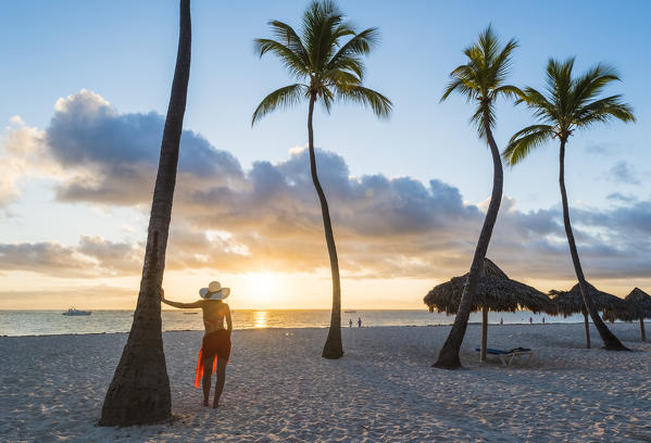 Bavaro Beach, Bavaro, Higuey, Punta Cana, Dominican Republic. Woman admiring the sunrise on a palm-fringed beach (MR).