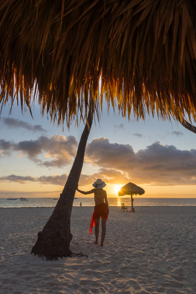 Bavaro Beach, Bavaro, Higuey, Punta Cana, Dominican Republic. Woman by thatch umbrellas on the beach at sunrise (MR).