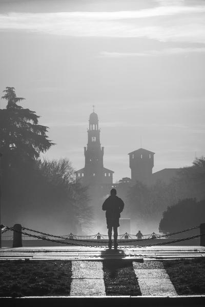 Milan, Lombardy, Italy. A man jogging with the Sforzesco Castle in the background