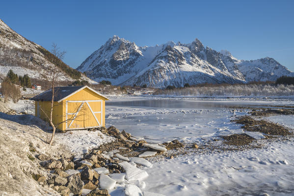 Yellow cabin with snowcapped mountains in the background. Vestpollen, Nordland county, Northern Norway region, Norway.