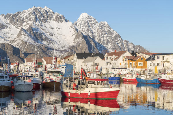 Fishing boats in the harbour, with snowcapped mountains in the background. Henningsvaer, Nordland county, Northern Norway region, Norway.