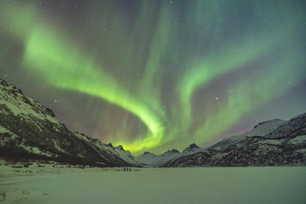 Northern lights with mountains and three people in winter. Kleppstad, Nordland county, Northern Norway, Norway.