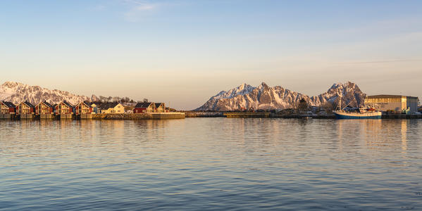 Traditional red houses and fishing boat at sunset in winter. Henningsvaer, Nordland county, Northern Norway region, Norway.