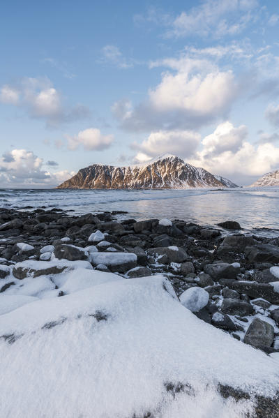 Skagsanden beach in winter, with rocks and snow in the foreground at sunset. Flakstad, Nordland county, Northern Norway, Norway.