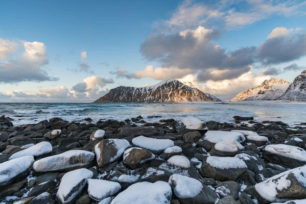 Skagsanden beach in winter, with rocks and snow in the foreground at sunset. Flakstad, Nordland county, Northern Norway, Norway.