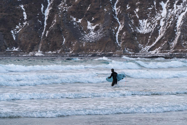 Man surfboarding in the sea in winter. Skagsanden beach, Flakstad, Nordland county, Northern Norway, Norway.