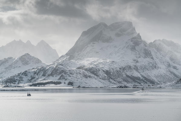 Fishing boat sailing on the fjord, with Narvtinden peak in the background in winter. Fredvang, Flakstad municipality, Nordland county, Northern Norway, Norway.