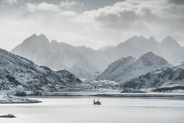 Fishing boat sailing on the fjord, with Tekoppstetten peak in the background in winter. Fredvang, Flakstad municipality, Nordland county, Northern Norway, Norway.