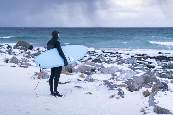Man with light blue surfboard standing and looking towards the sea. Skagsanden beach, Flakstad, Nordland county, Northern Norway, Norway.