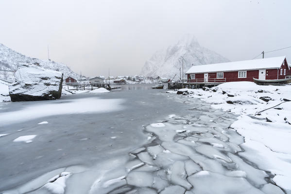 Frozen fjord with red cabin and Olstinden peak in the background. Reine, Nordland, Northern Norway, Norway.