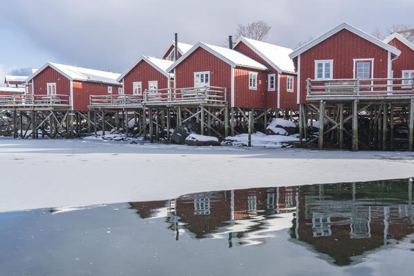 Traditional 'rorbu' houses reflected on the frozen fjord. Reine, Lofoten district, Nordland county, Northern Norway, Norway.