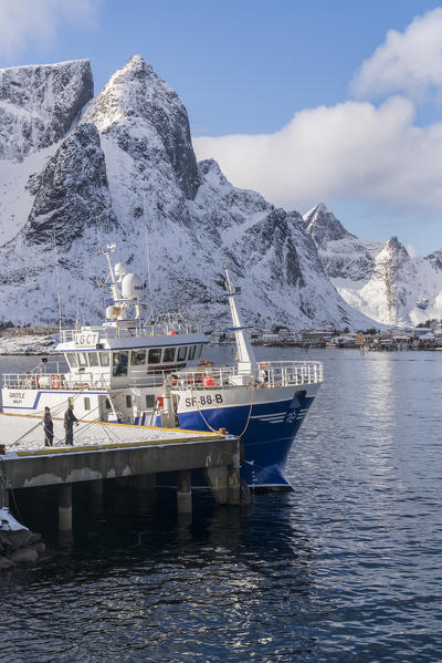 Fishing boat at the harbour with Navaren peak covered in snow in the background. Reine, Nordland county, Northern Norway region, Norway.