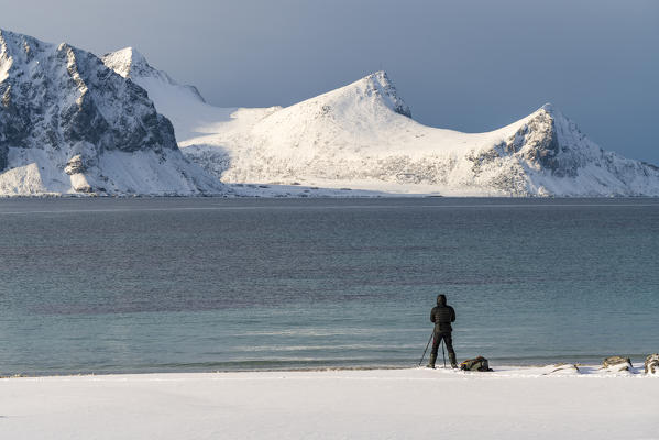 Man standing taking pictures of the mountains from Haukland Beach in winter. Leknes, Nordland county, Northern Norway, Norway.