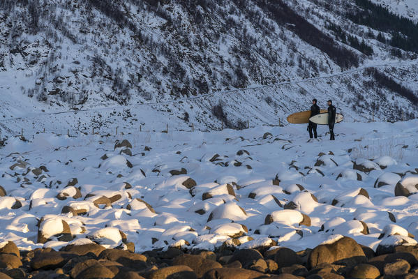 Two surfers with their surfboards standing on Unstad Beach in winter. Vestvagoy municipality, Nordland county, Northern Norway, Norway.