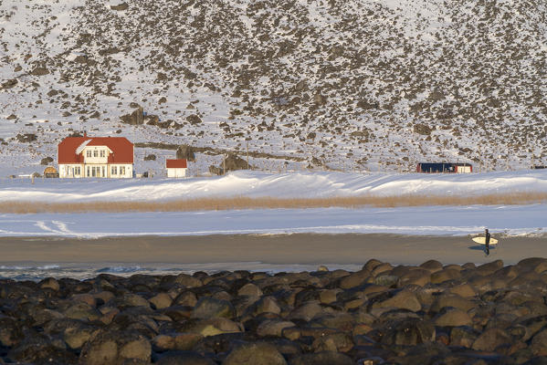 Surfer walking on Unstad Beach in winter. Vestvagoy municipality, Nordland county, Northern Norway, Norway.