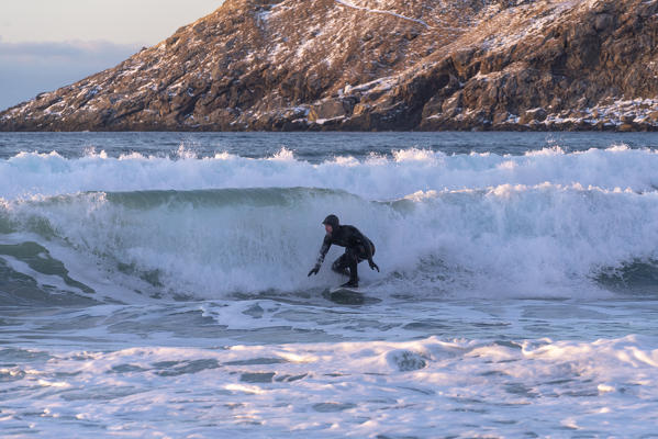 Man surfing at Unstad Beach in winter. Vestvagoy municipality, Nordland county, Northern Norway, Norway.