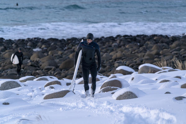 Two surfers walking on Unstad Beach in winter. Vestvagoy municipality, Nordland county, Northern Norway, Norway.