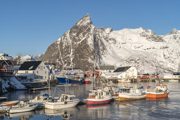 Fishing boats in the harbour of Hamnoy in winter, with Olstinden peak in the background. Reine, Nordland county, Northern Norway, Norway.