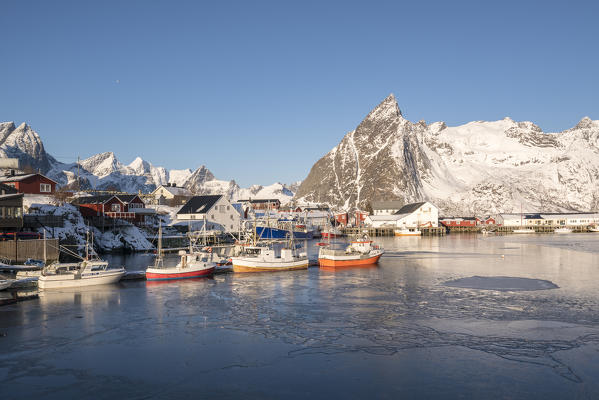 Fishing boats in the harbour of Hamnoy in winter, with Olstinden peak in the background. Reine, Nordland county, Northern Norway, Norway.
