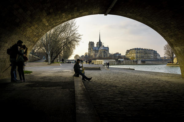 Two lovers kissing and a musician under a bridge along seine river, near Notre Dame, Paris, France.