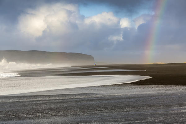 A man is walking towards the rainbow on the beach of Reynisfjara, Vik, Sudurland, Iceland, Europe