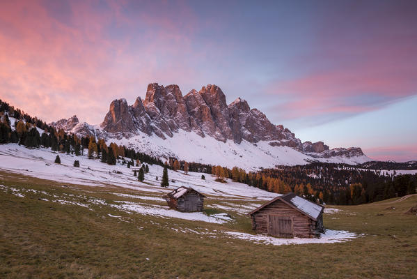 Sunrise with two wooden lodges and Odle Dolomites. Malga Gampen, Funes, Bolzano, Trentino Alto Adige - Sudtirol, Italy, Europe.