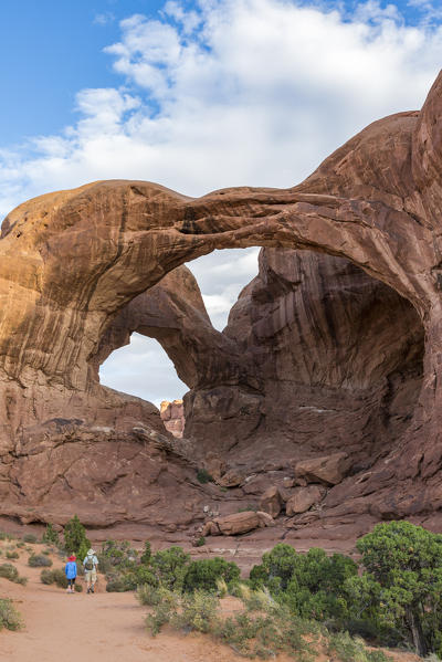 Two people in front of Double Arch. Arches National Park, Moab, Grand County, Utah, USA.