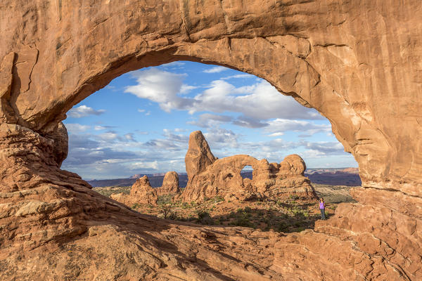Woman under North Window with Turret Arch on the background. Arches National Park, Moab, Grand County, Utah, USA.