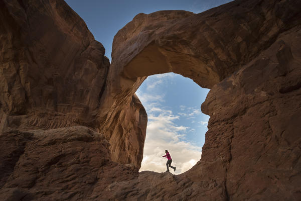 Girl playing under Double Arch. Arches National Park, Moab, Grand County, Utah, USA.