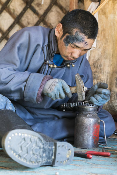 Nomadic boy fixing his motorbike's chain. Bayandalai district, South Gobi province, Mongolia.