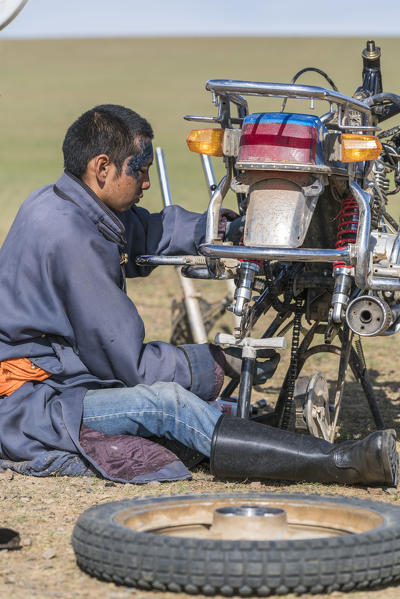 Nomadic boy fixing his motorbike. Bayandalai district, South Gobi province, Mongolia.