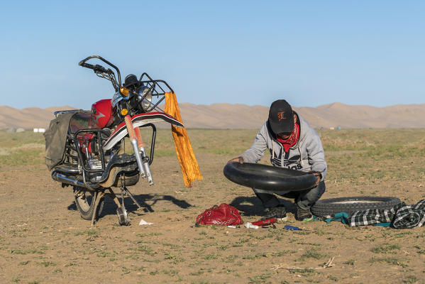 Nomadic man fixing the tire of his motorbike. Sevrei district, South Gobi province, Mongolia.